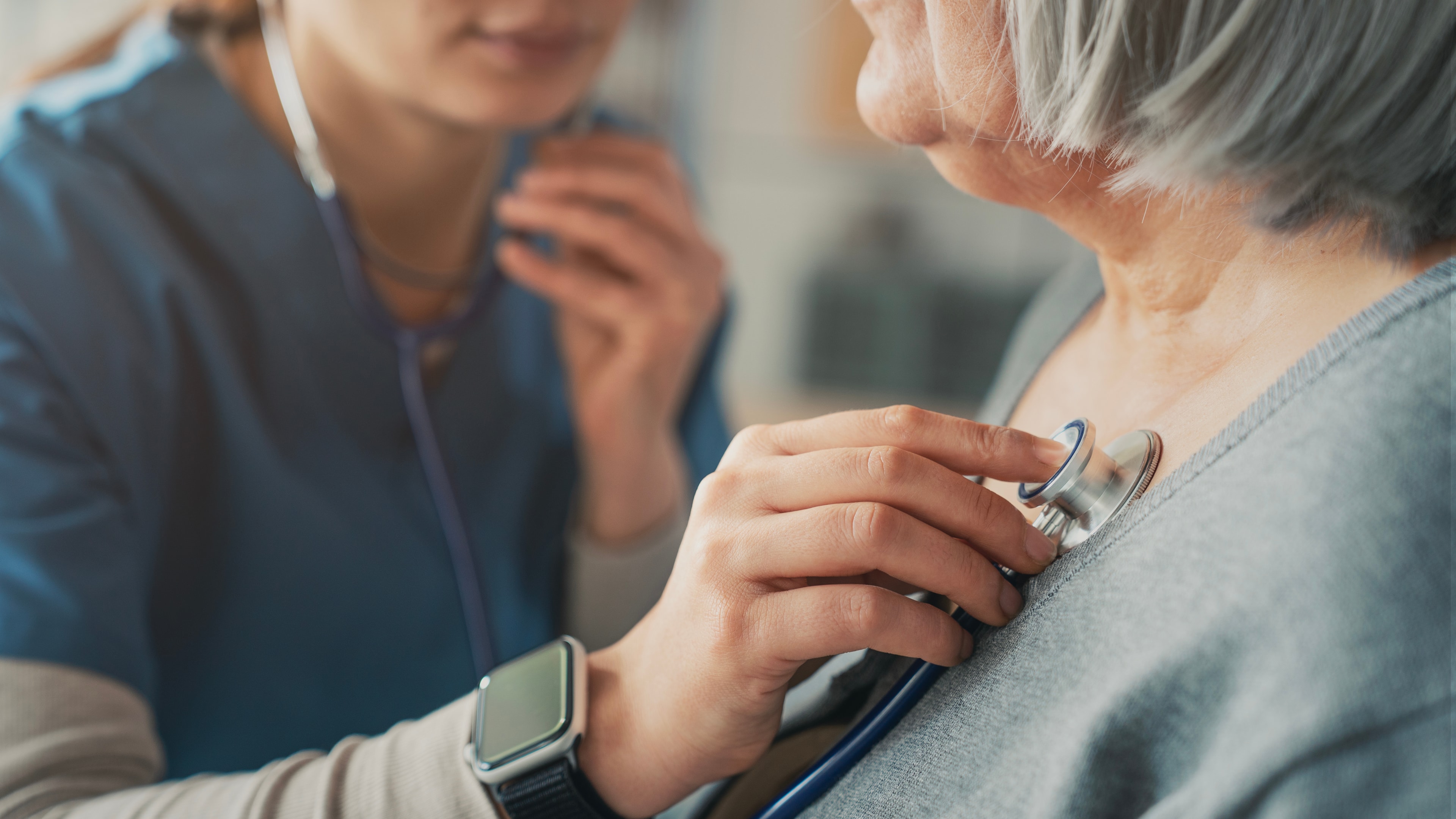 Hospice nurse examining senior patient with stethoscope during home visit